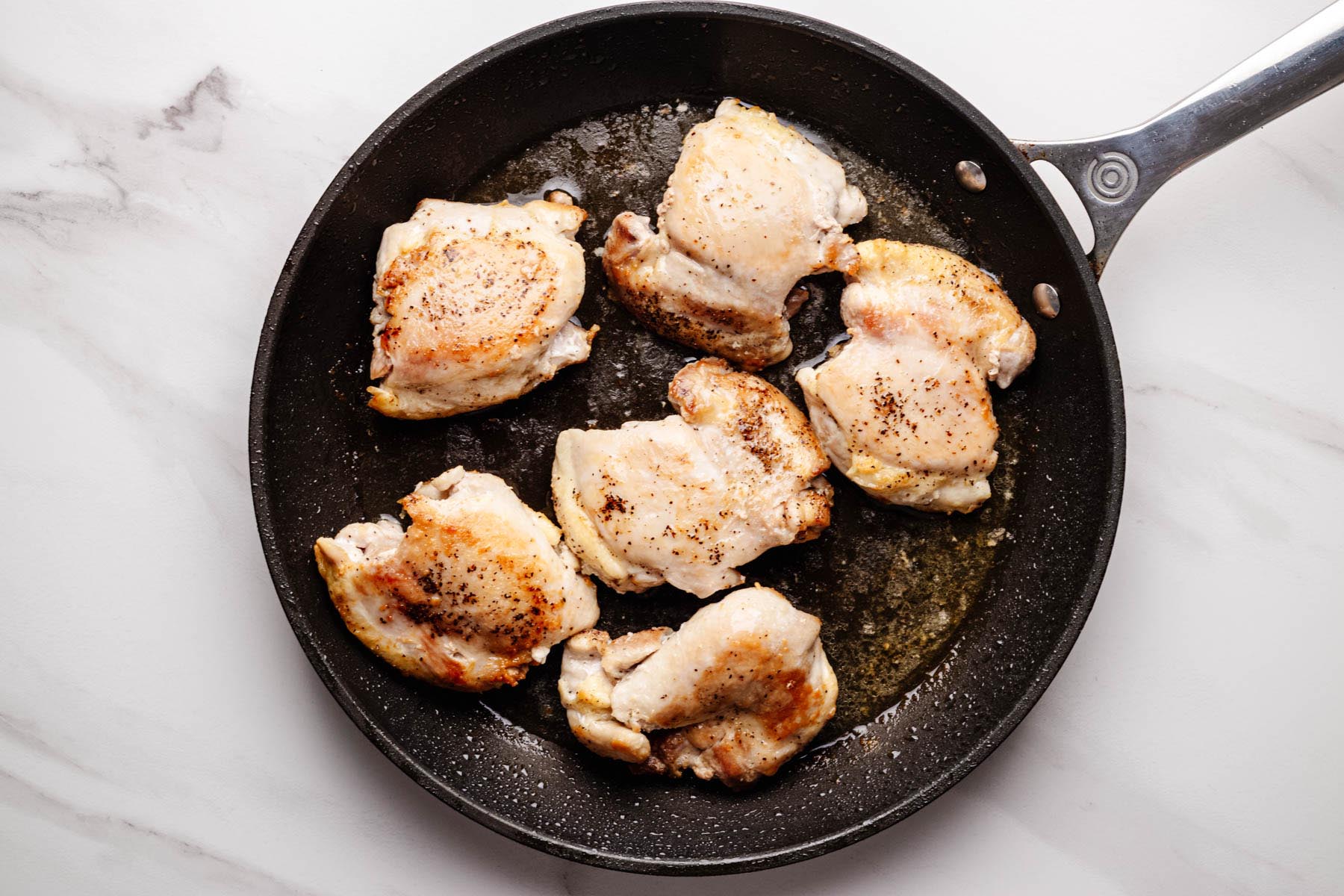 Chicken thighs searing in a black skillet until golden brown.