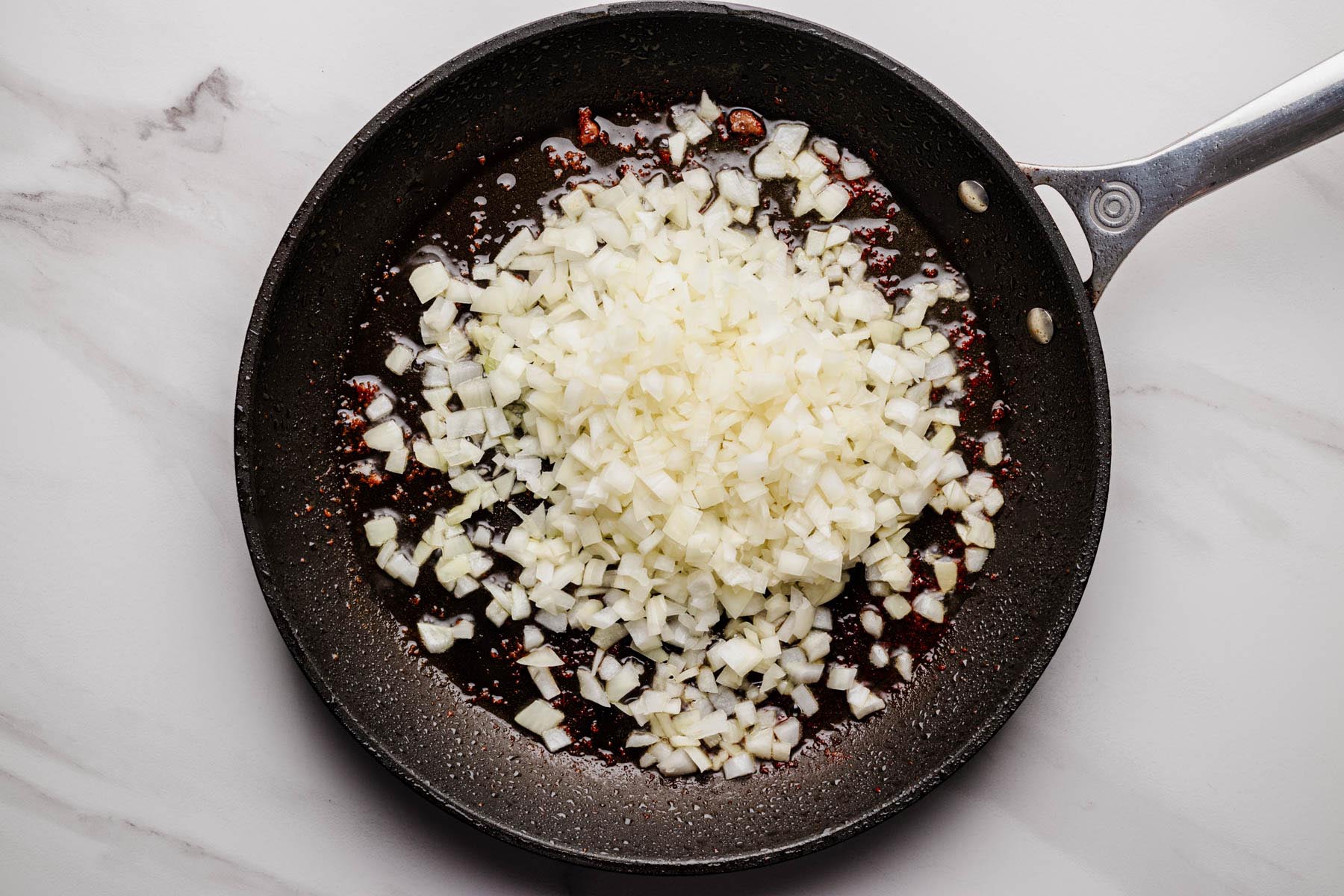 Diced onions saut&eacute;ing in a skillet with oil and browned bits.