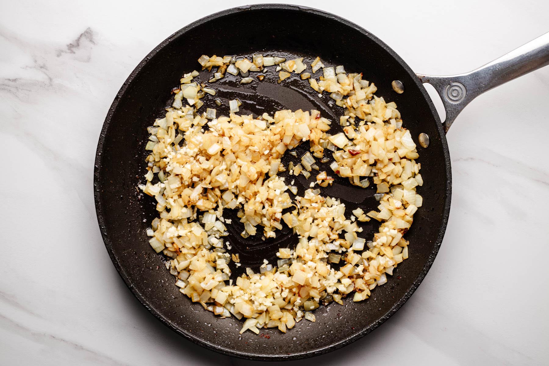 Saut&eacute;ed onions with minced garlic cooking in a skillet.