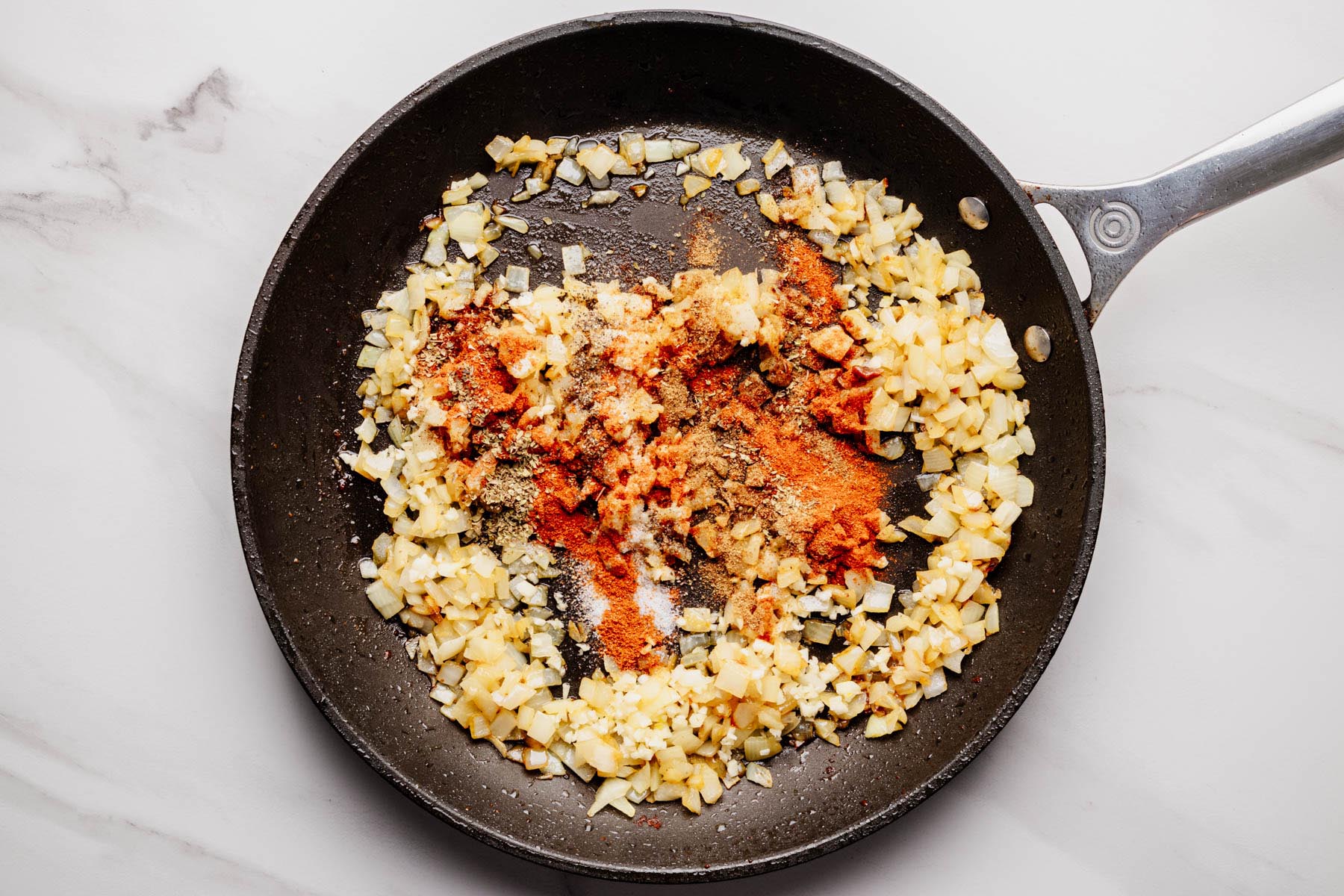 Saut&eacute;ed onions and garlic in a skillet with added spices sprinkled on top.