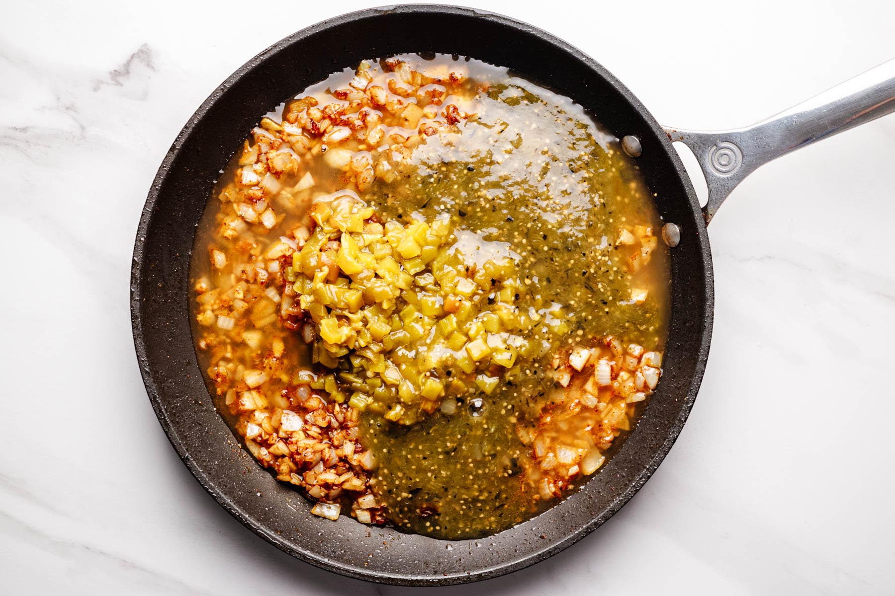 Skillet filled with saut&eacute;ed onions, spices, chicken broth, salsa verde, and fire-roasted green chiles.
