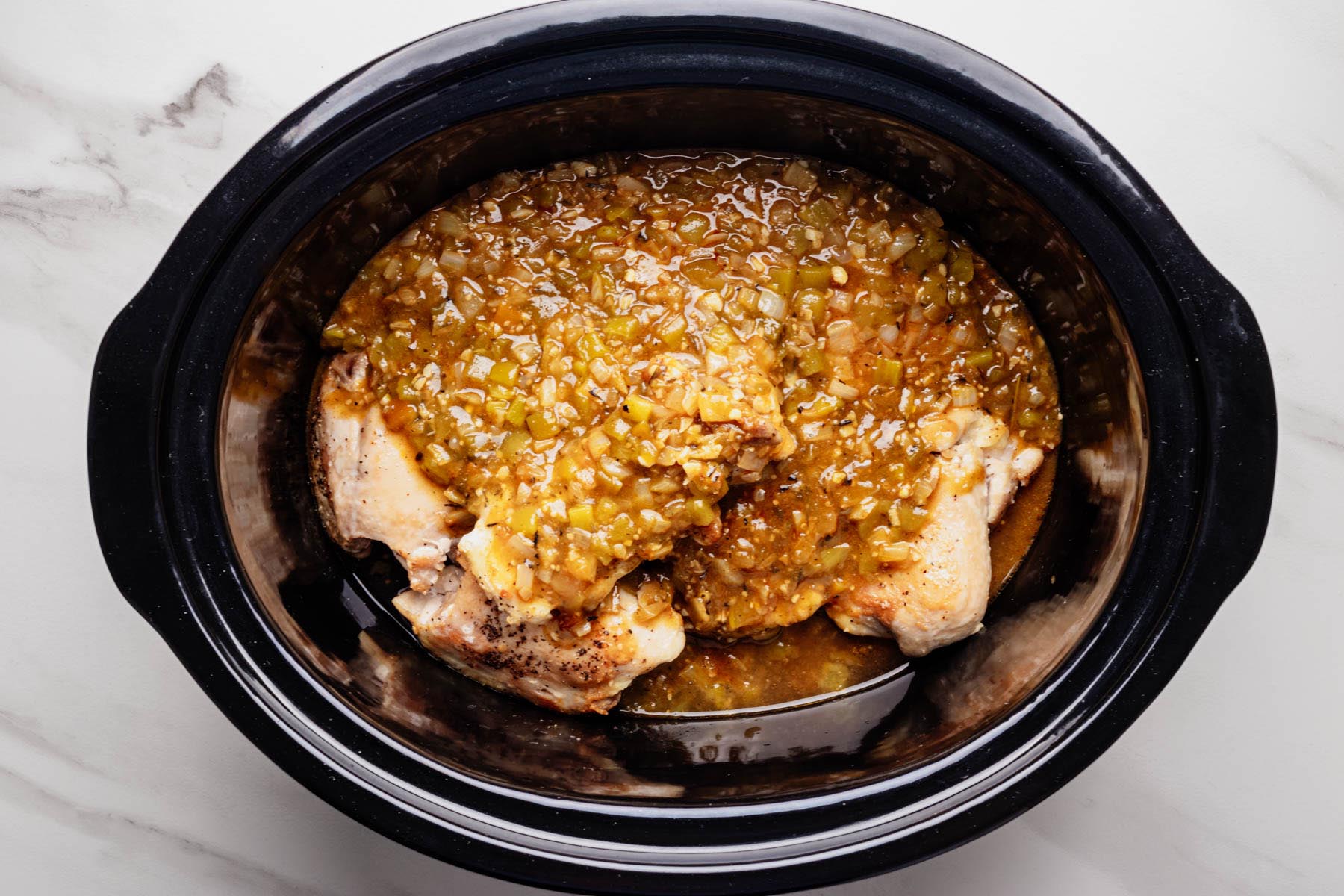 Seared chicken thighs in a slow cooker covered with a green chili, onion, and salsa verde sauce.