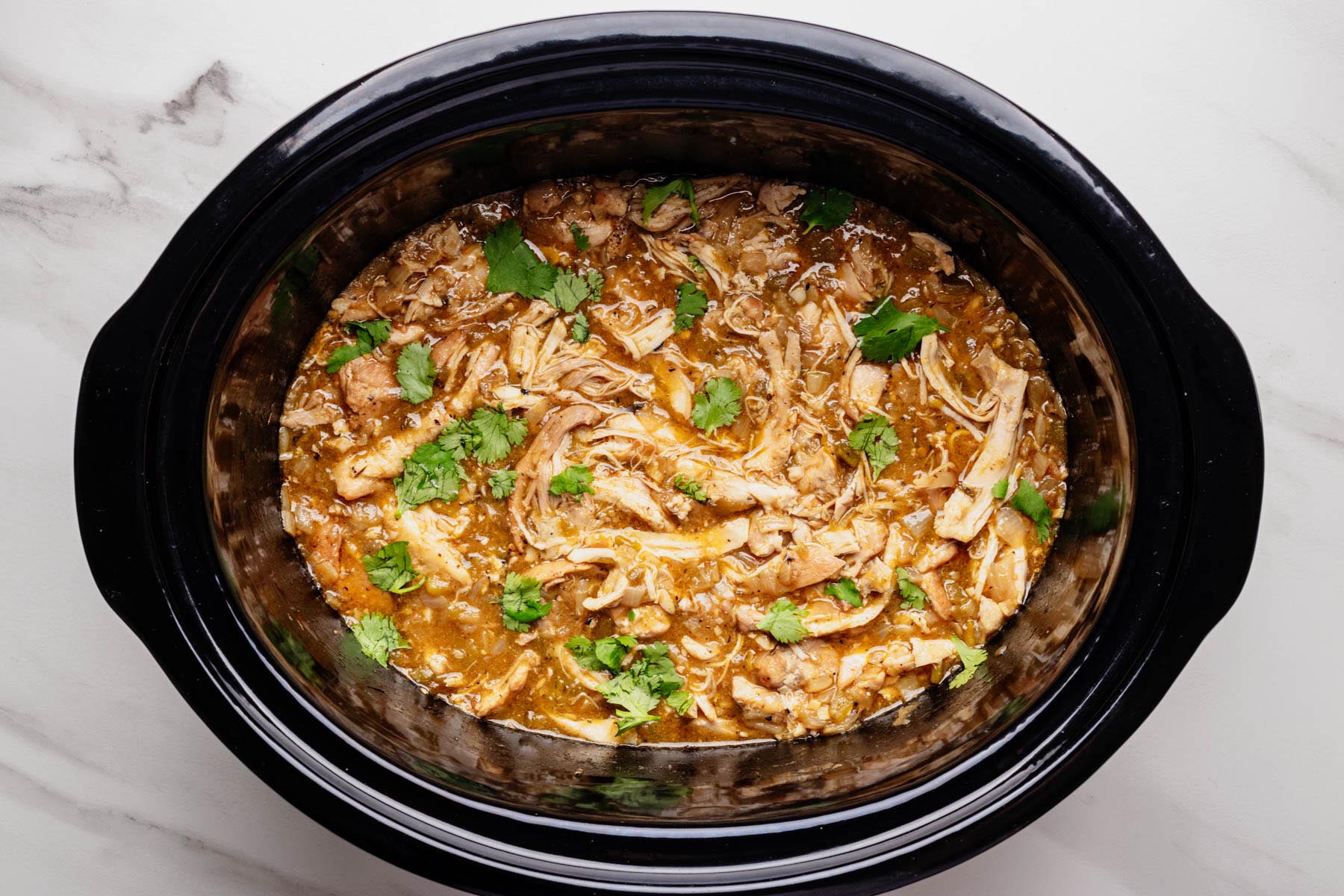 Shredded green chili chicken in a slow cooker topped with fresh cilantro.