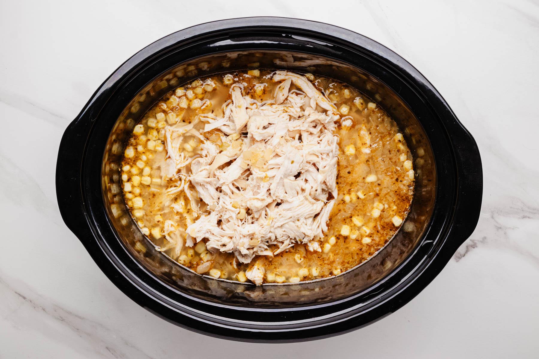Shredded cooked chicken added back into the slow cooker with corn and spiced broth—ready to finish the white chicken chili.