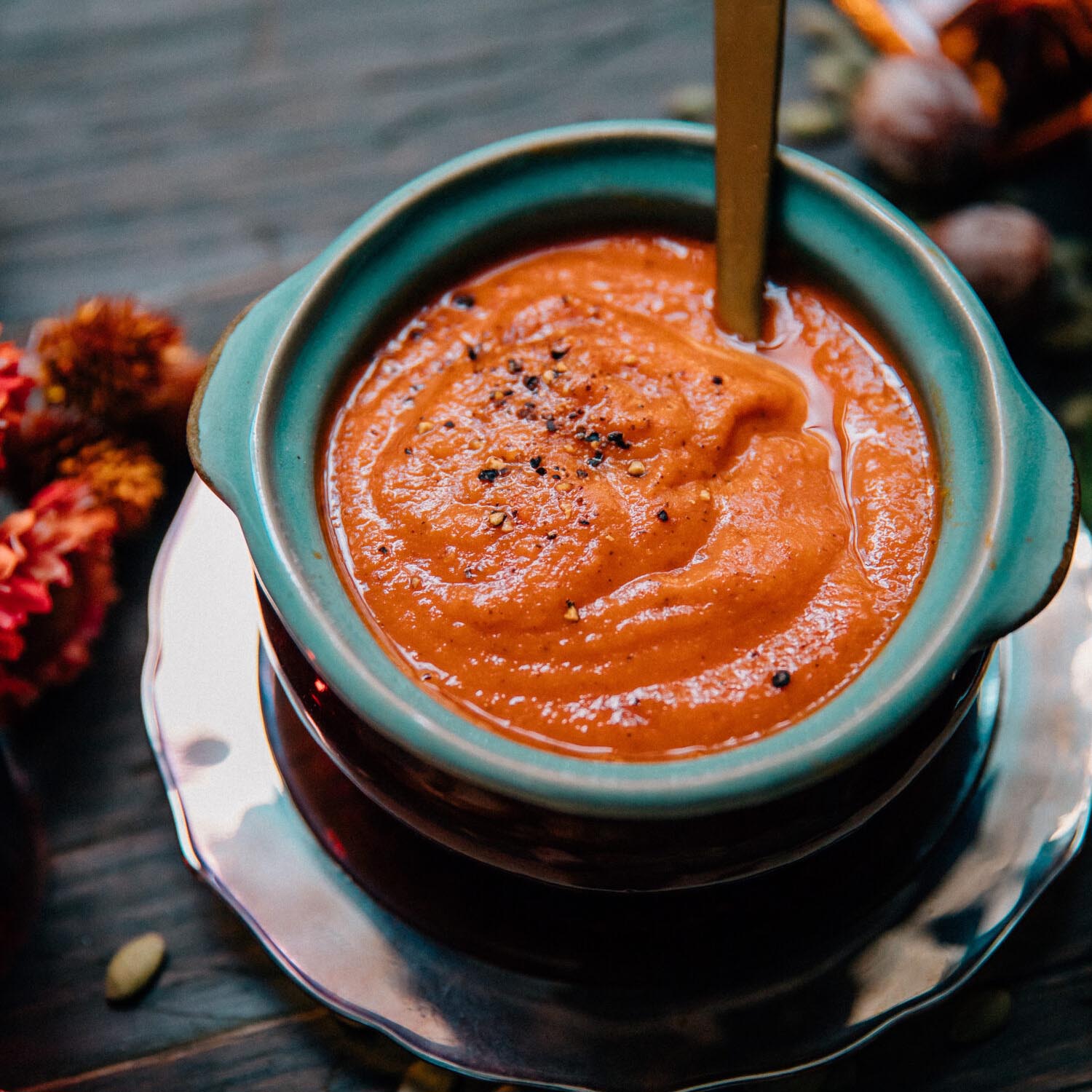 Silky pumpkin tomato soup in a rustic teal bowl with cracked pepper.