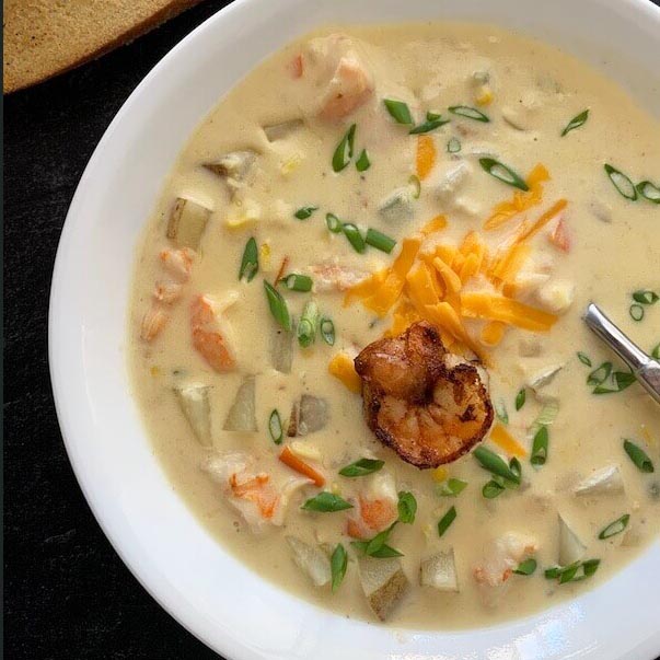 Creamy shrimp and corn soup with potatoes, scallions, cheddar, and a seared shrimp on top.