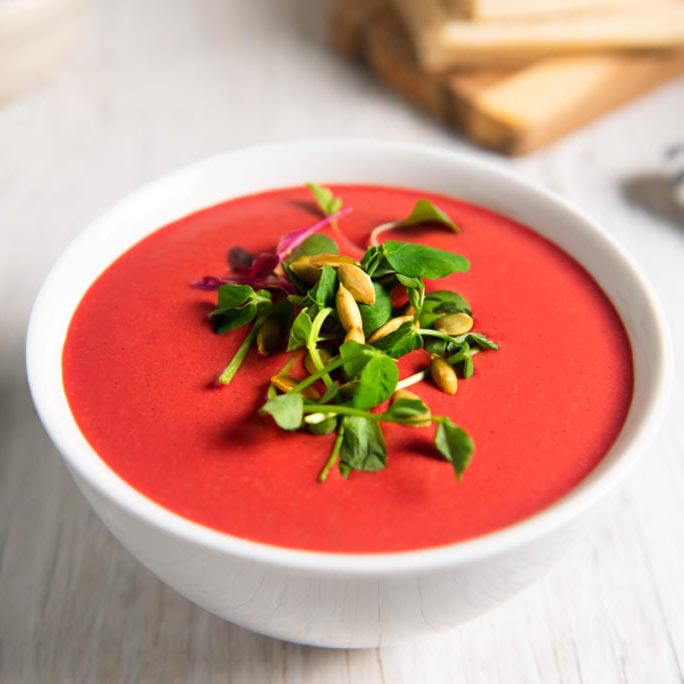 Silky beet soup in a white bowl, garnished with microgreens and pumpkin seeds.