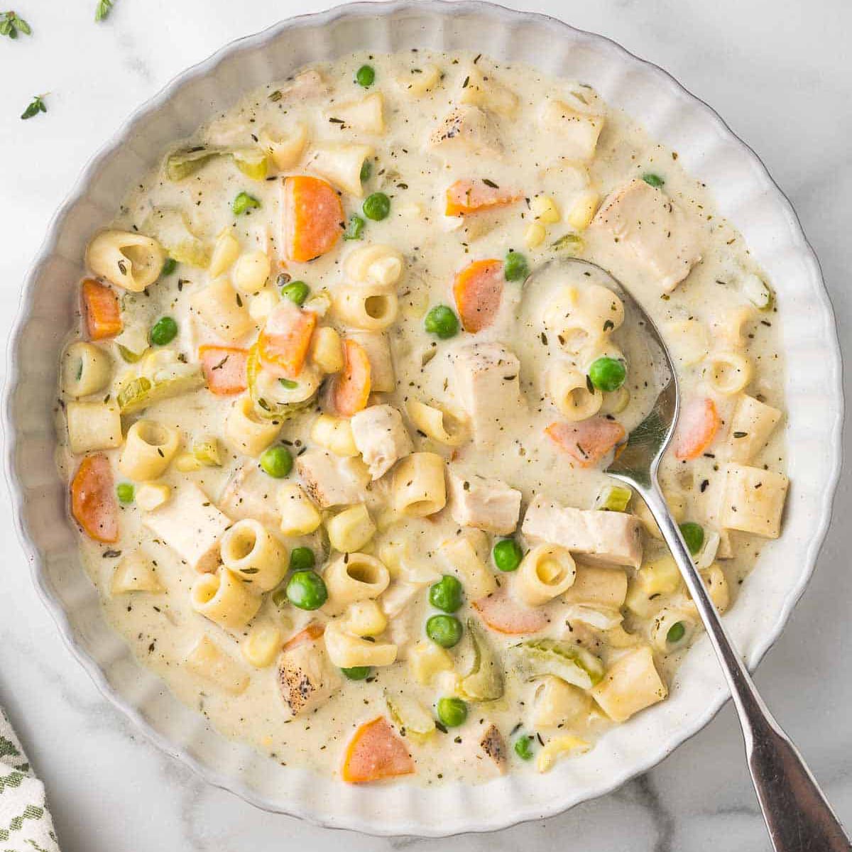 Creamy chicken and vegetable soup with ditalini, carrots, peas, and celery in a white bowl.