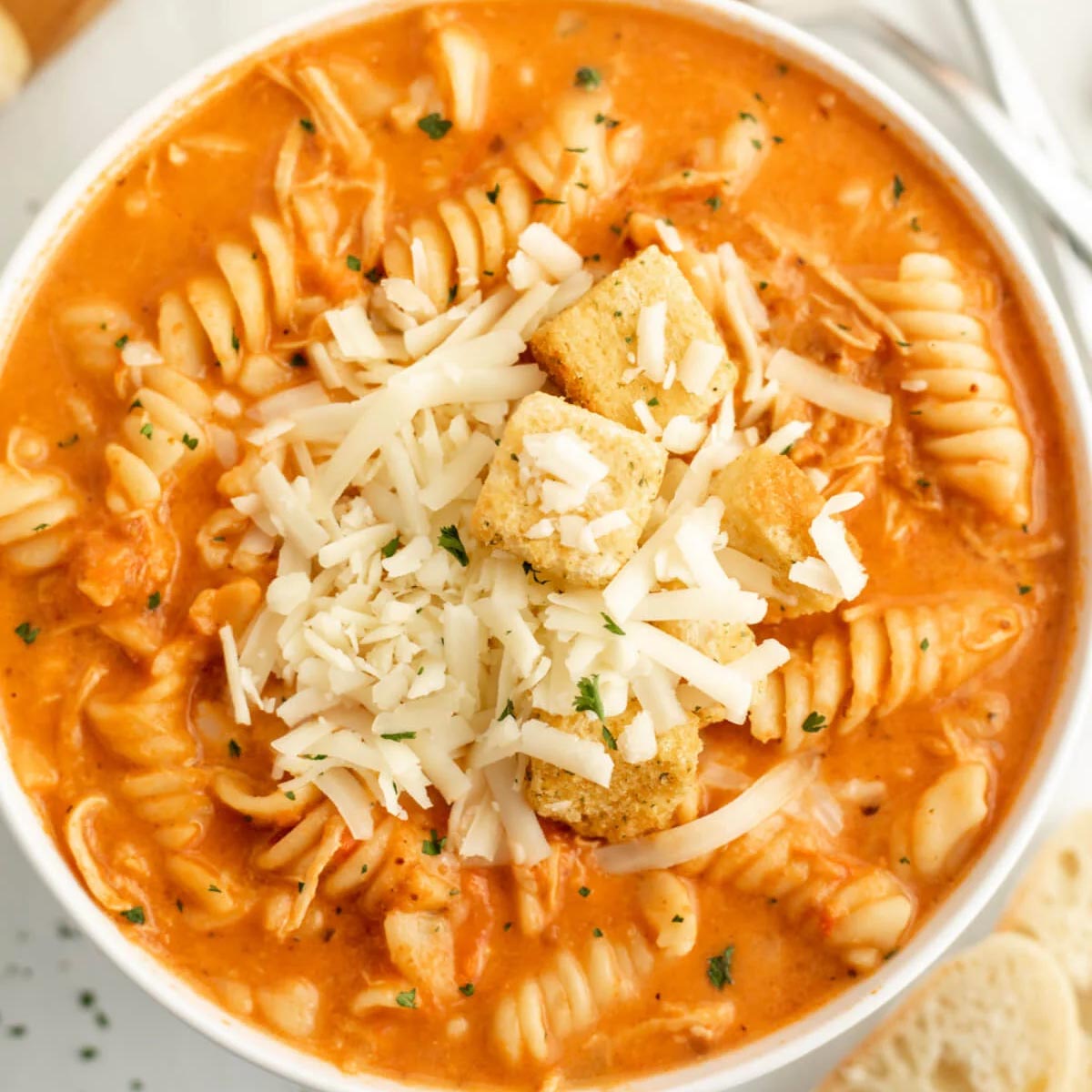 Creamy Crockpot chicken Parmesan soup with rotini pasta, topped with shredded cheese and croutons.