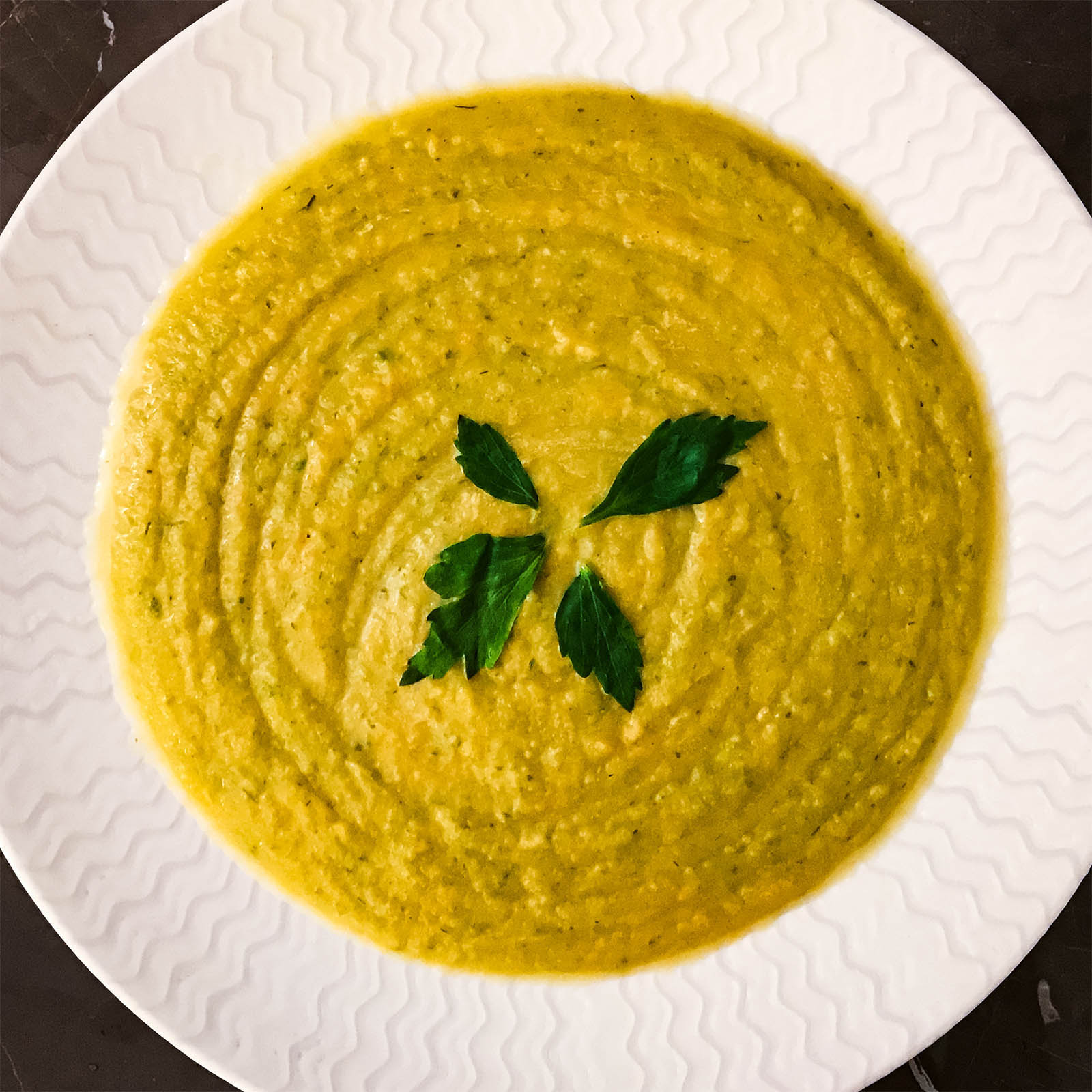 Creamy autumn vegetable soup in a white bowl, garnished with three parsley leaves.