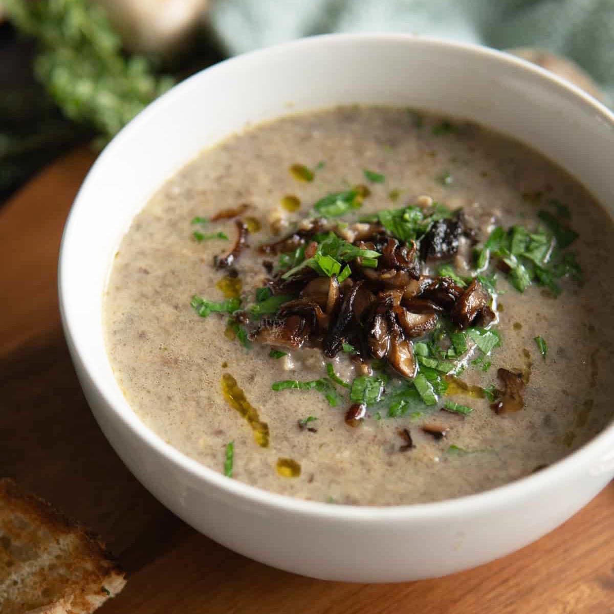 Creamy mushroom soup with saut&eacute;ed mushrooms and chopped parsley in a white bowl.