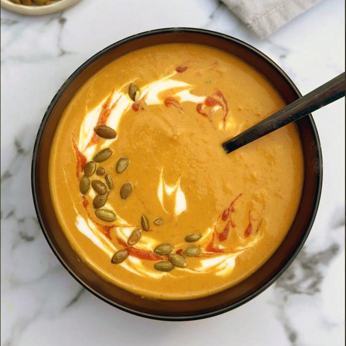 Pumpkin spice soup with a yogurt swirl, chili oil, and pepitas in a black bowl.