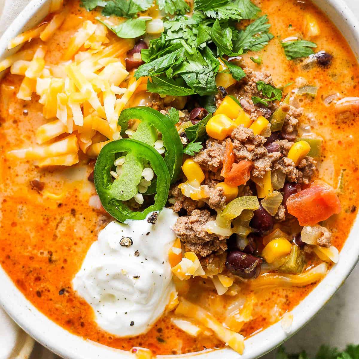 Creamy taco soup with ground beef, corn, black beans, and tomatoes; topped with jalape&ntilde;o, cilantro, cheese, and sour cream.