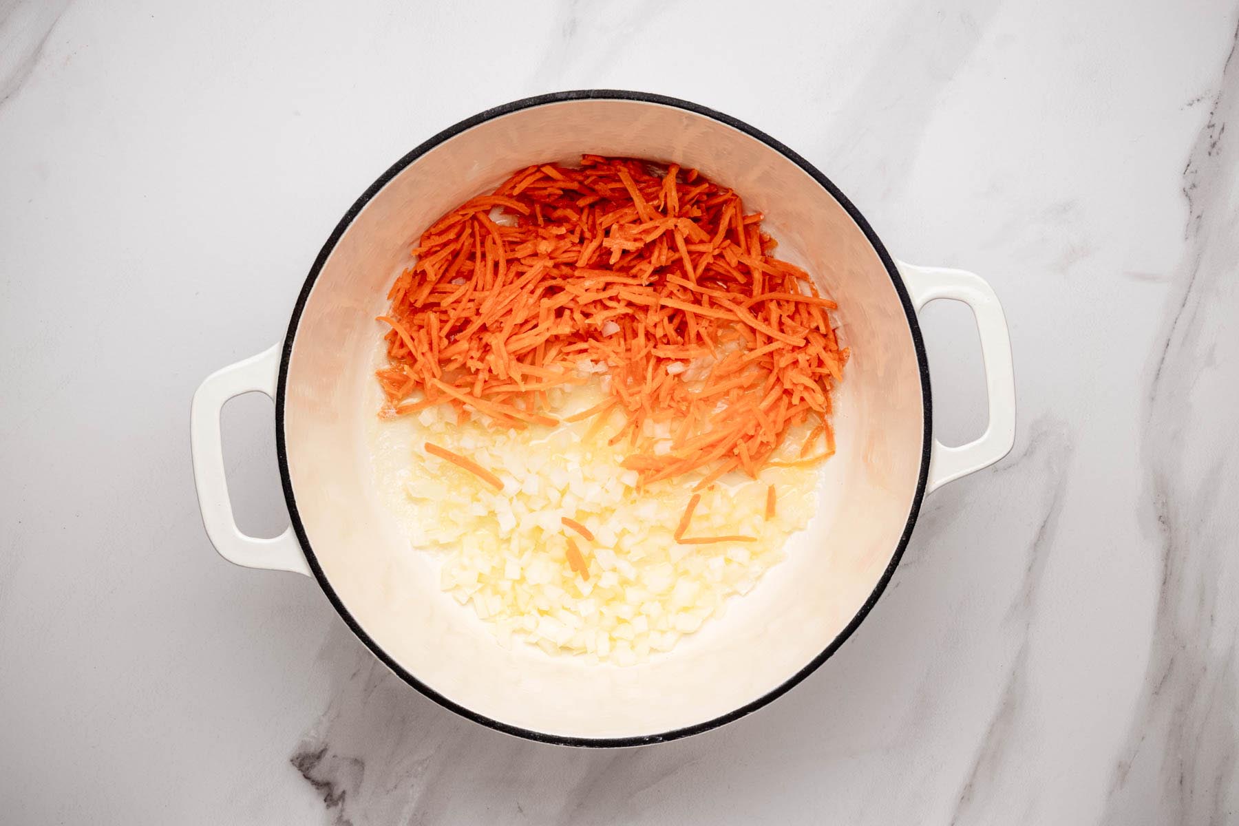 Dutch oven with melted butter, diced onion, and shredded carrots starting to sauté for broccoli cheddar soup.