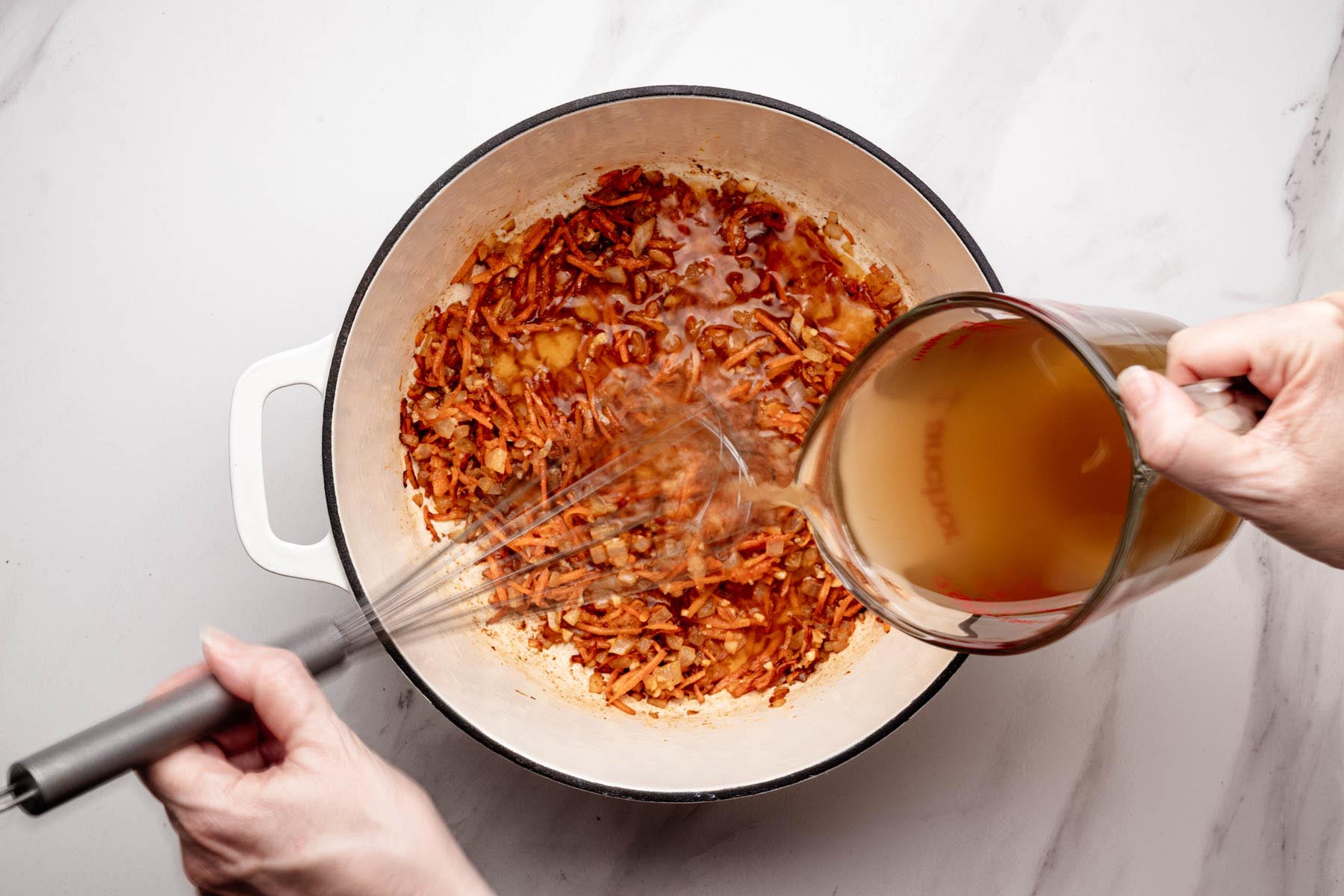 Whisking while pouring chicken stock into a Dutch oven of sautéed carrots and onions to deglaze.