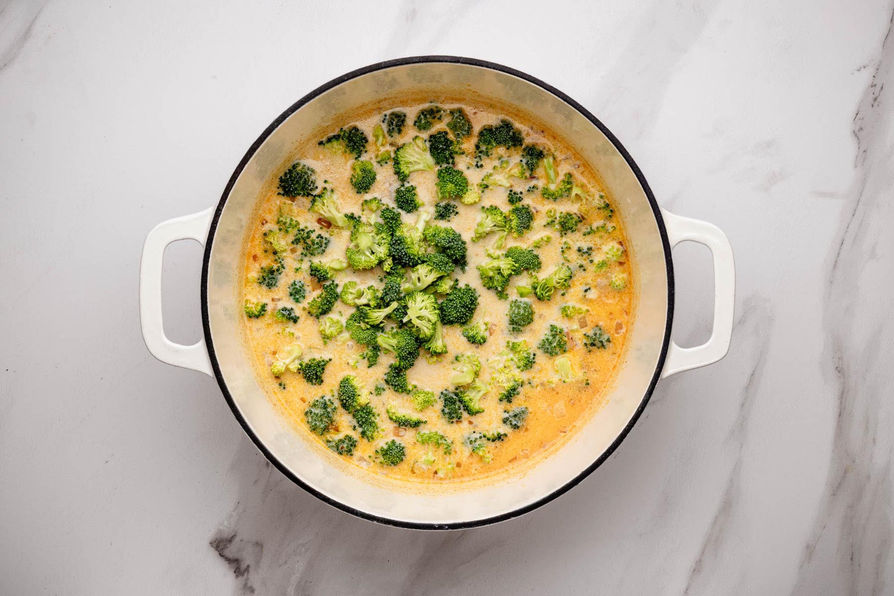 Fresh broccoli florets simmering in a creamy soup base in a Dutch oven after adding the slurry.