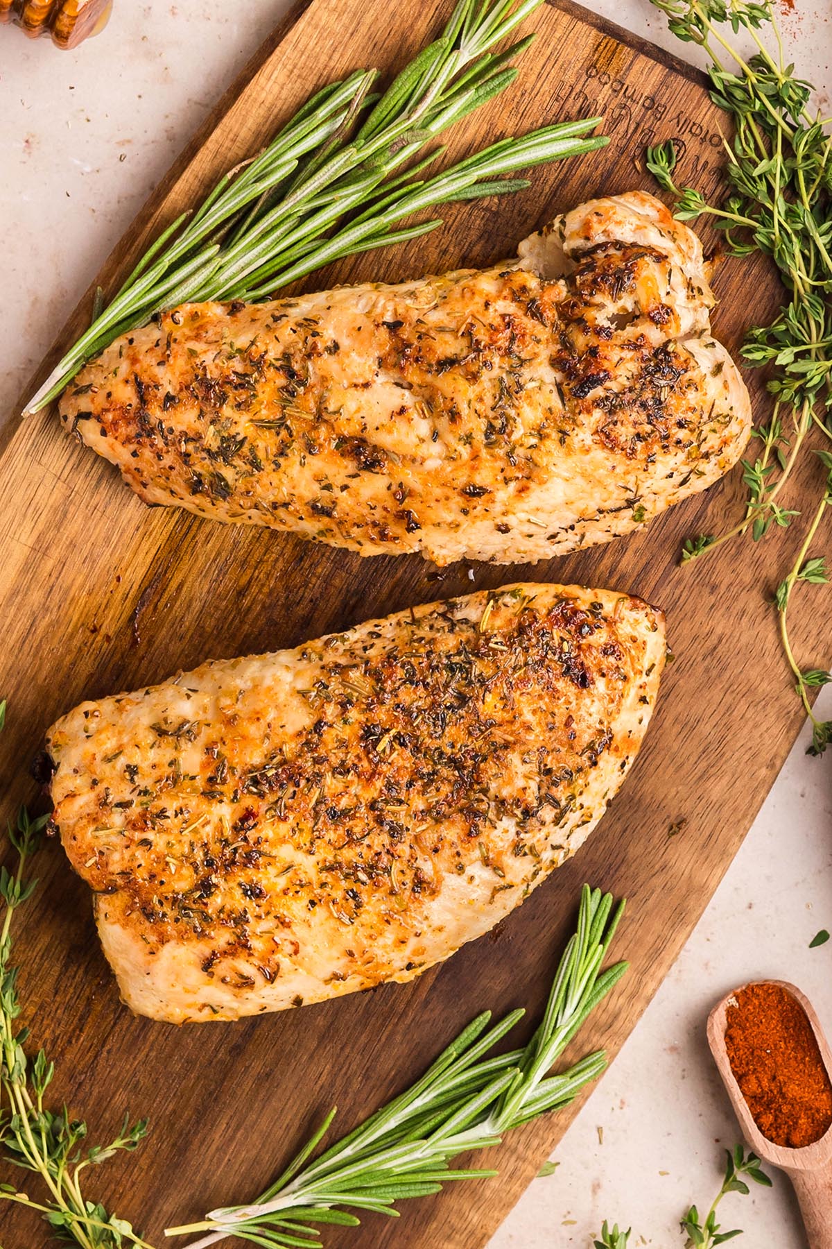 Herb-roasted turkey breast tenderloins resting on a wooden board before slicing, with rosemary and thyme.
