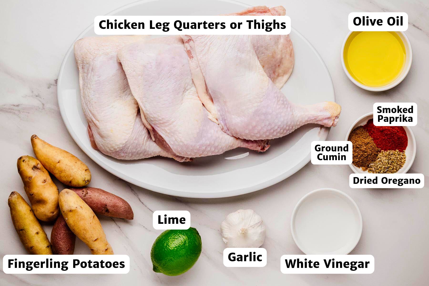 Raw chicken leg quarters on a white plate with ingredients for Peruvian marinade—fingerling potatoes, lime, garlic, white vinegar, olive oil, and small bowls of smoked paprika, ground cumin, and dried oregano—arranged on a marble surface with labeled callouts.