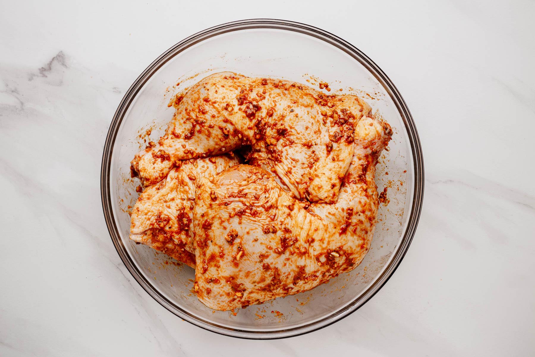 Chicken leg quarters coated in a paprika-garlic marinade in a glass bowl, ready to marinate.