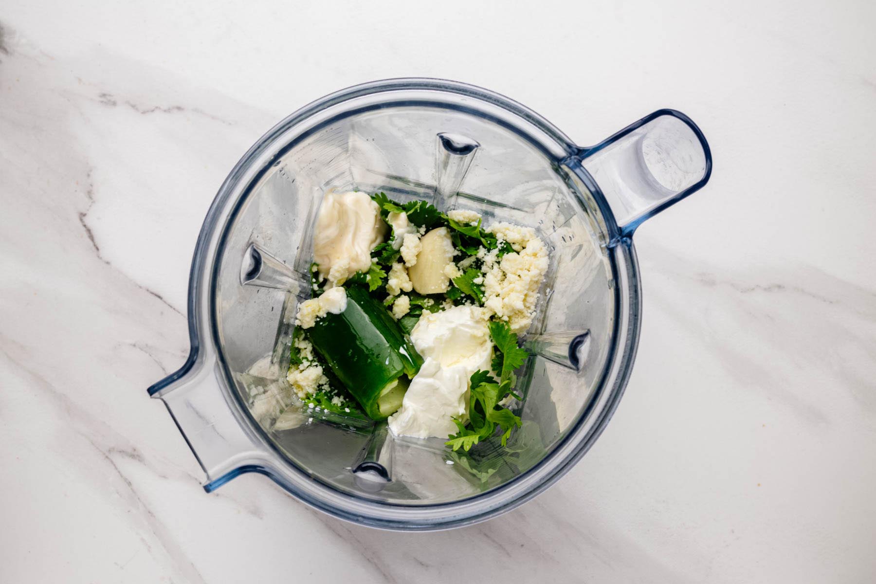 Blender jar with ingredients for aji verde—cilantro, jalapeño, garlic, cotija cheese, mayonnaise, and sour cream—ready to blend.