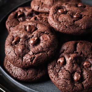 Close-up of double-chocolate peanut butter cookies arranged on a dark plate, highlighting their soft texture and glossy chocolate chips.
