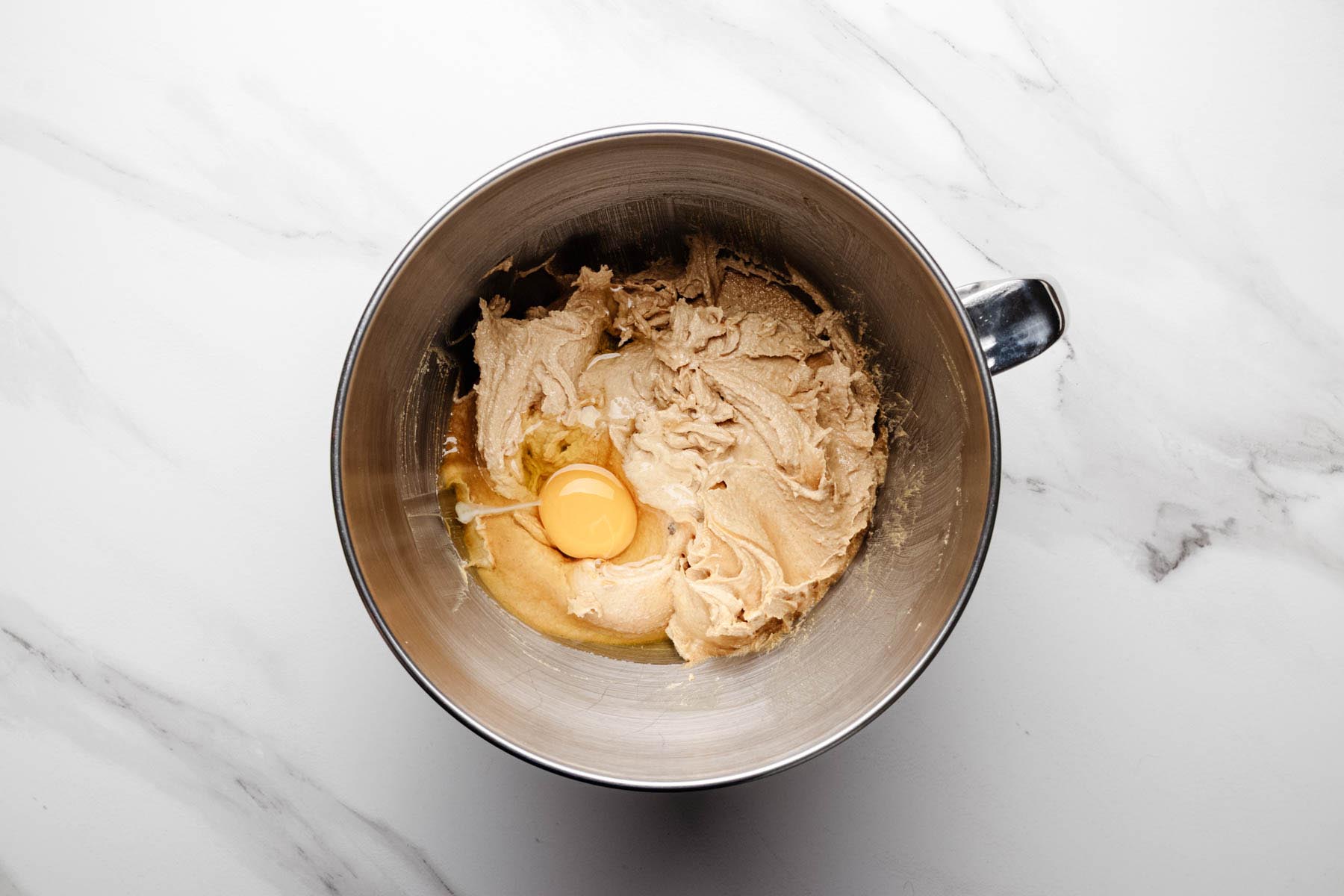 Creamed butter, peanut butter, and sugars in a mixer bowl with one egg just added on top of the mixture.