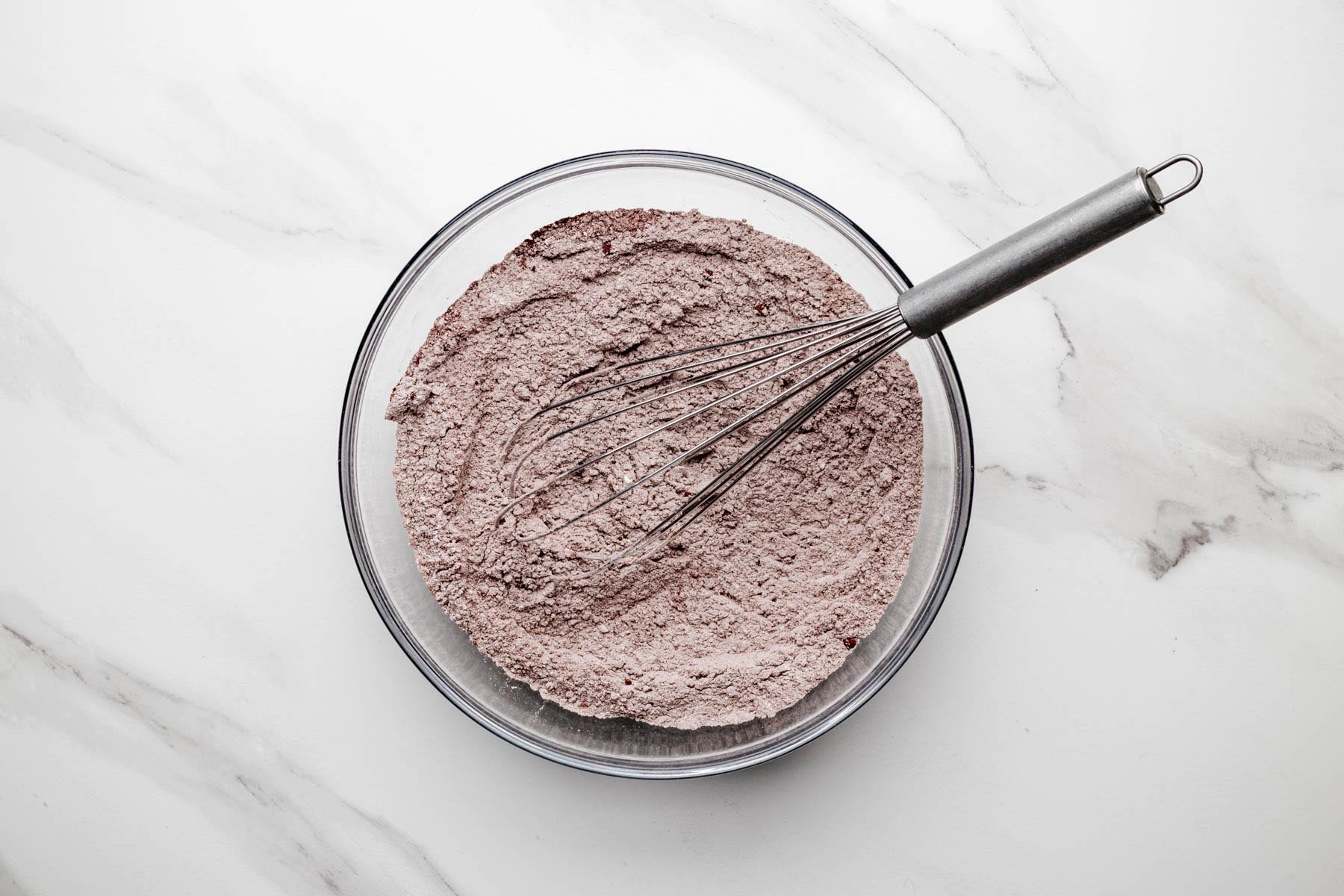 Whisked cocoa-flour mixture in a glass bowl with a metal whisk resting on top.