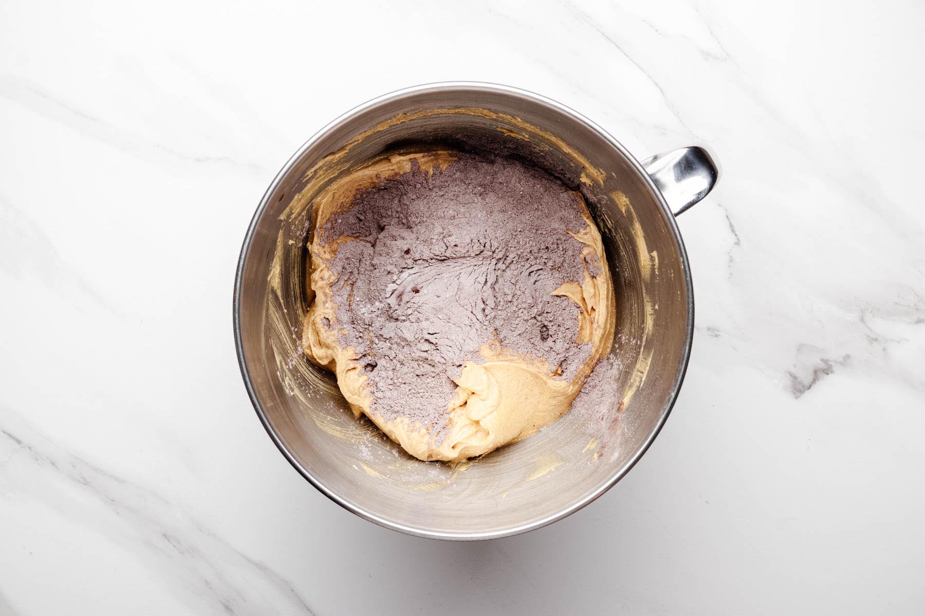 Partially mixed peanut butter cookie dough in a stand mixer bowl with the cocoa-flour mixture added on top.