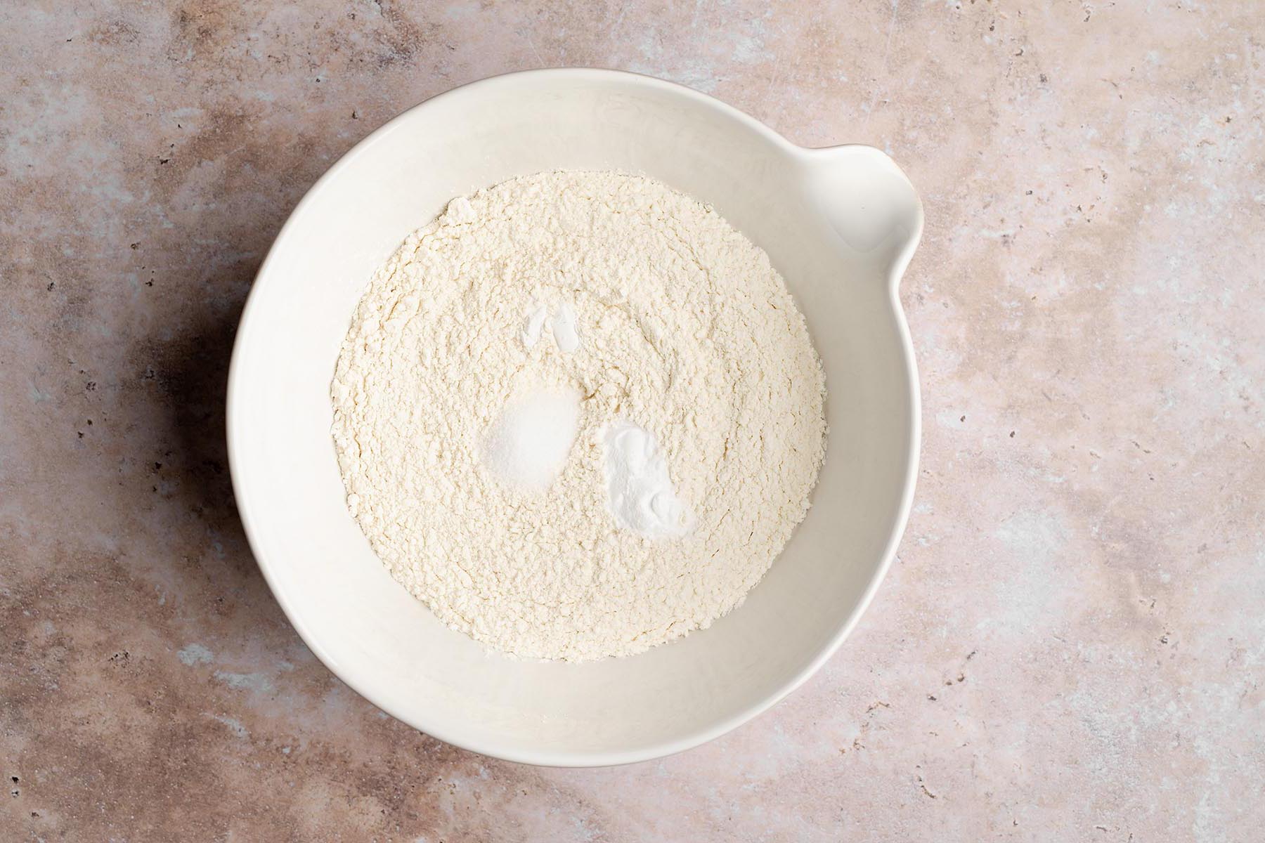 White mixing bowl with flour, baking soda, baking powder, and salt mounded together before whisking.