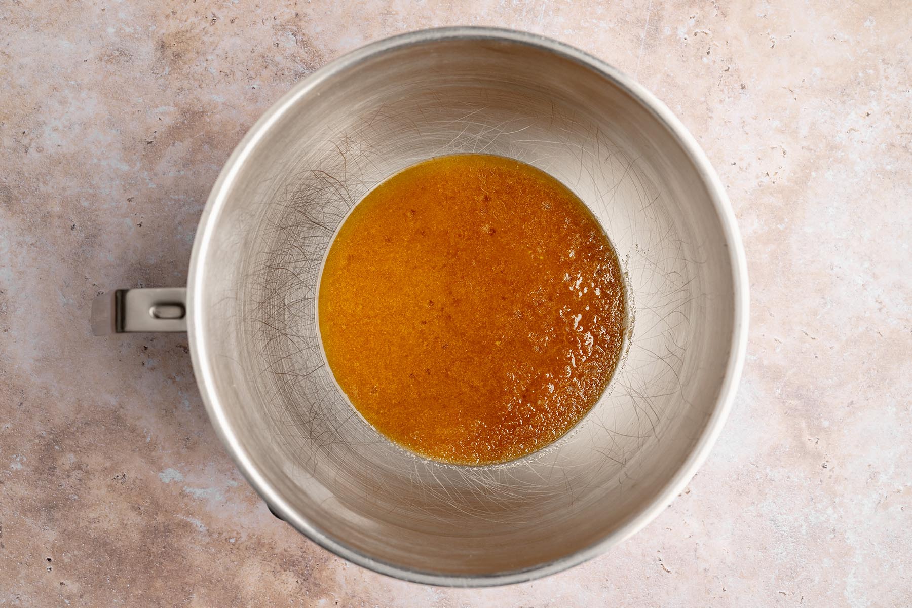 Browned butter and sugars mixed together in a metal bowl, forming a smooth amber-colored mixture.