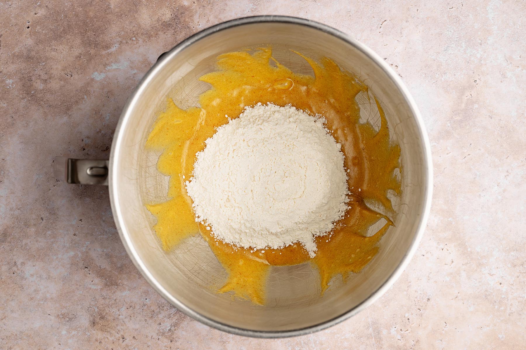 Flour mixture added on top of the wet ingredients in a mixing bowl, ready to be folded together.