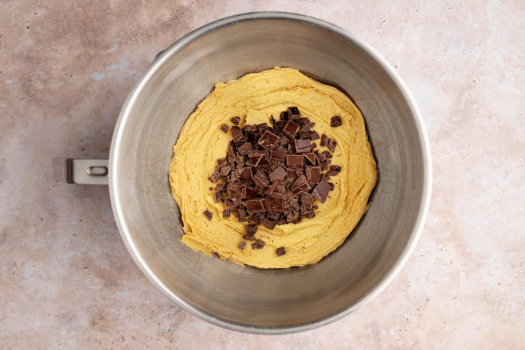 Chunky semi-sweet chocolate pieces piled on top of the mixed cookie dough in a metal bowl.