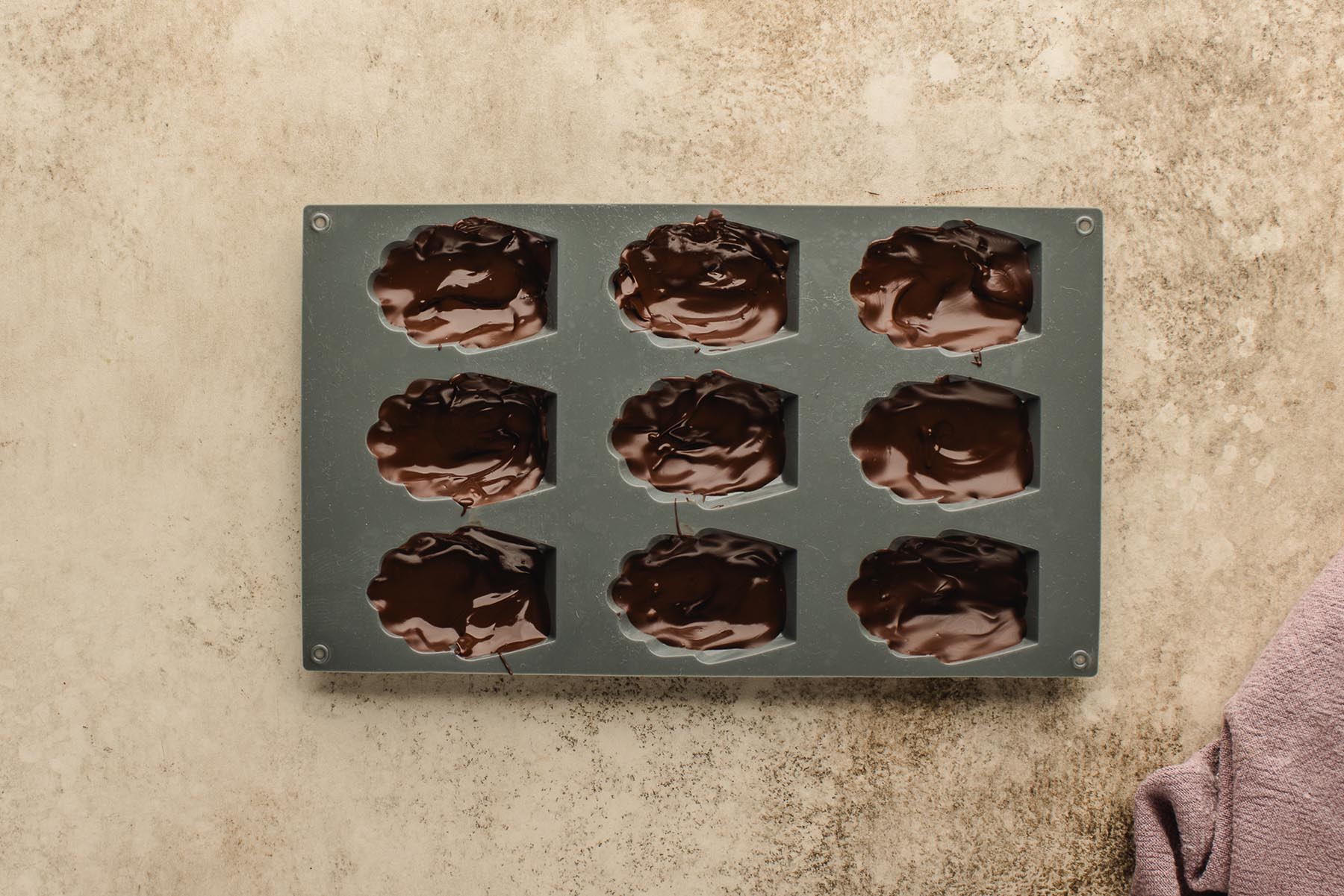 Madeleine wells filled with melted dark chocolate for dipping and setting.