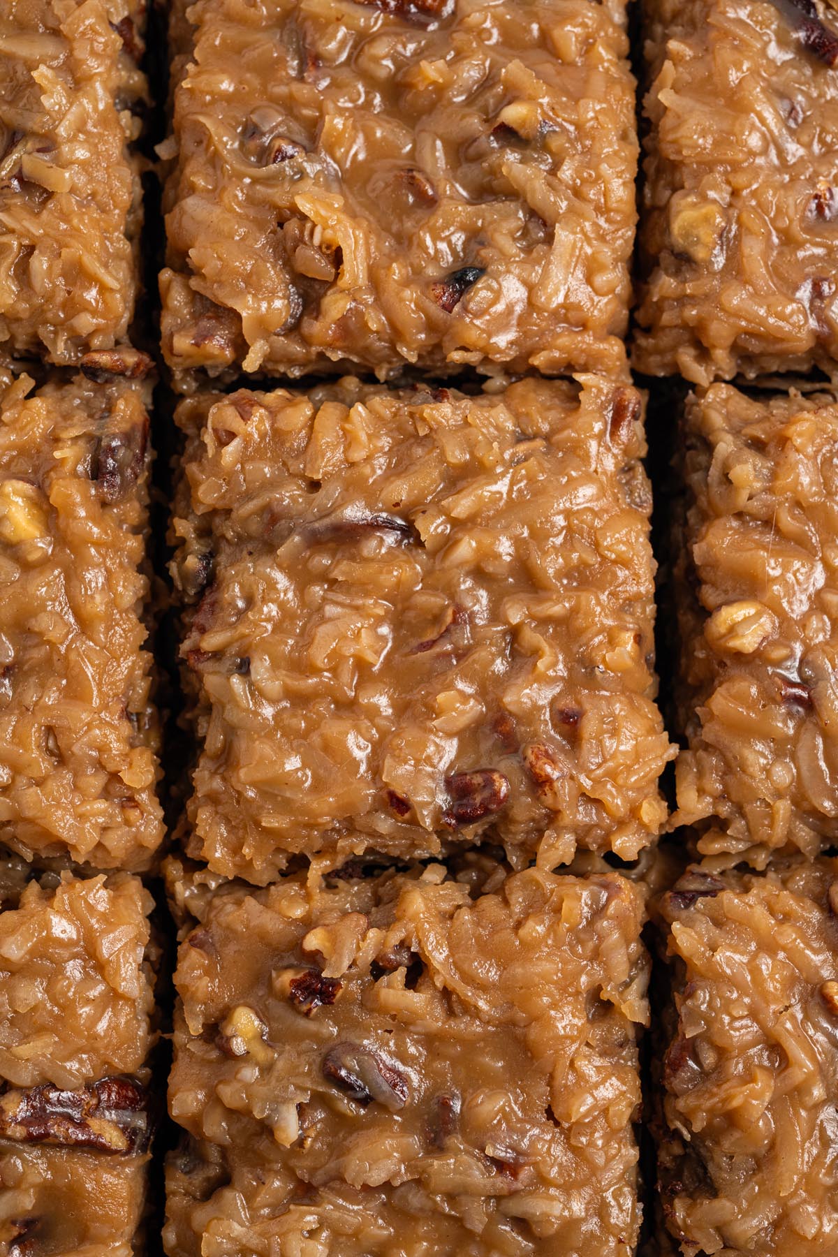 Overhead close-up of German chocolate brownies cut into neat squares, highlighting the glossy coconut-pecan topping with visible coconut shreds and pecan pieces.