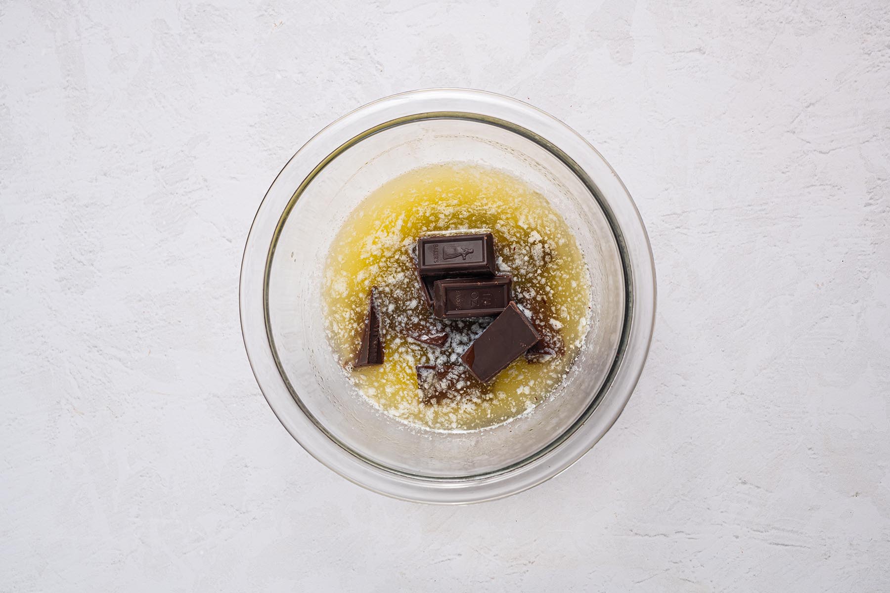 Chopped German baking chocolate added to hot melted butter in a glass bowl before stirring.