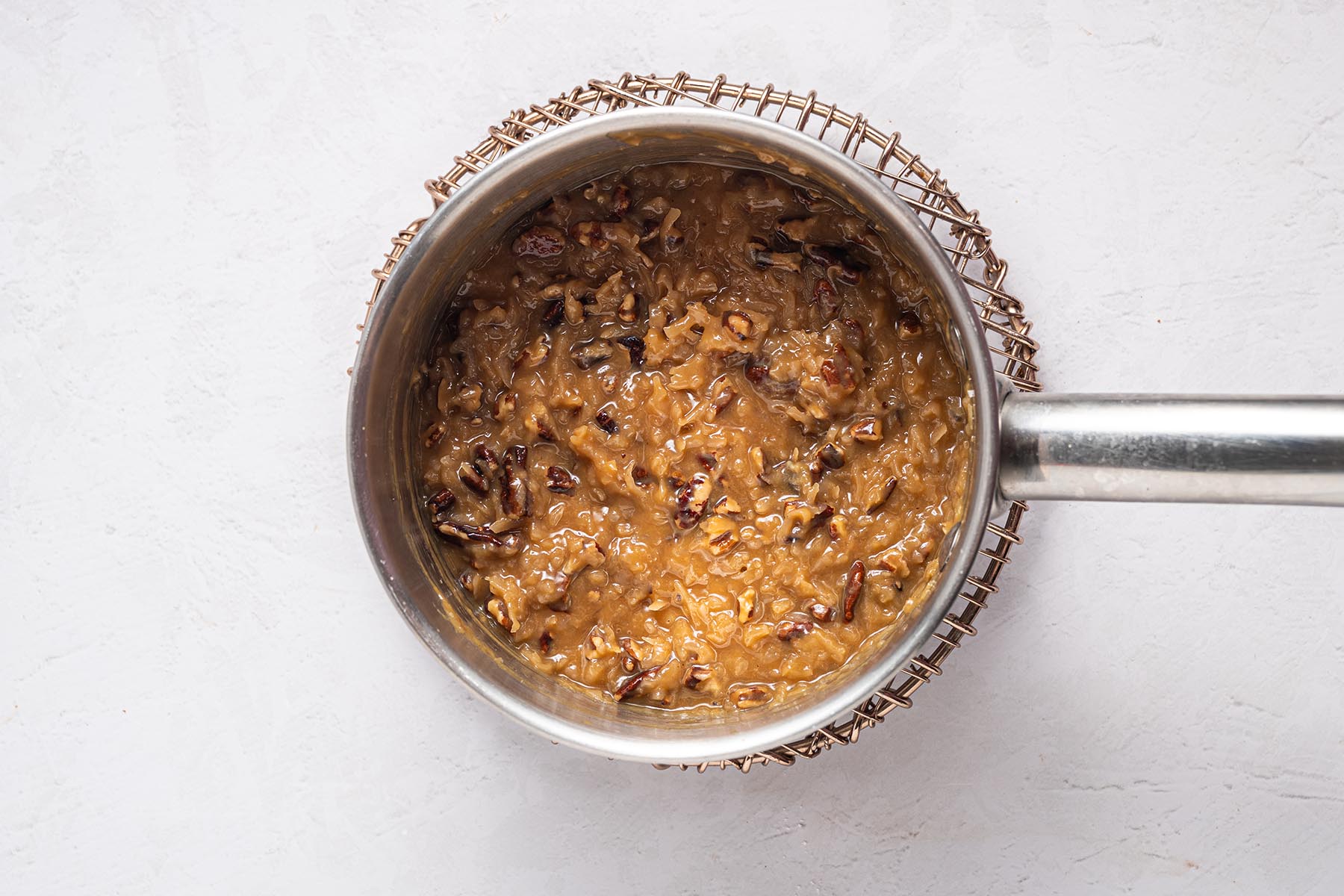 Coconut-pecan frosting finished in the saucepan—thick, glossy, and studded with chopped pecans.