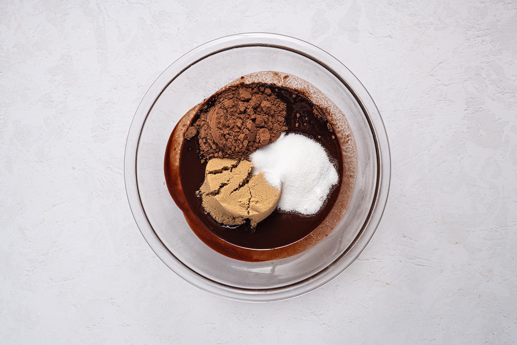 Cocoa powder, brown sugar, and granulated sugar sitting on the warm chocolate-butter mixture.