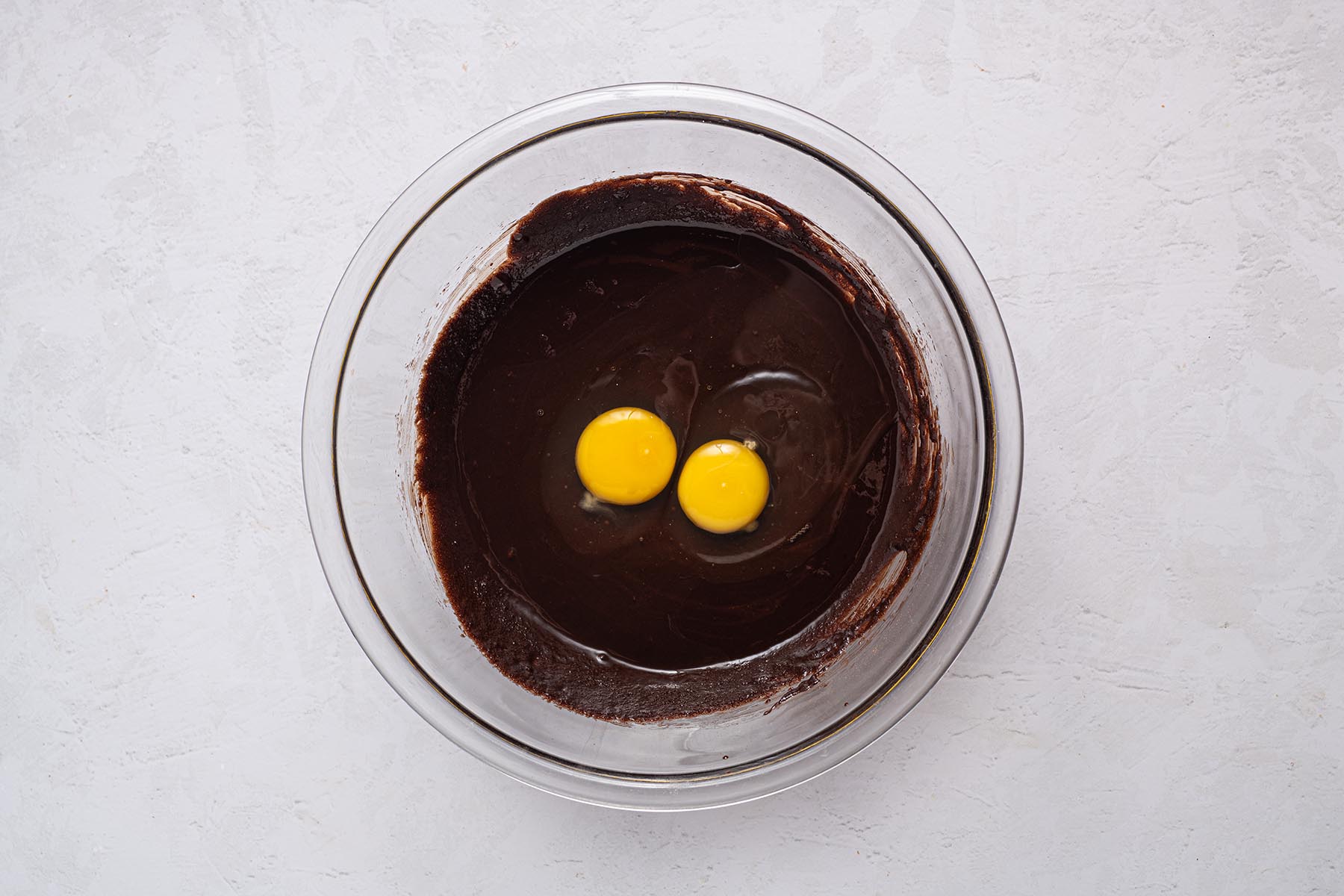 Two room-temperature eggs cracked into the glossy chocolate mixture before whisking.