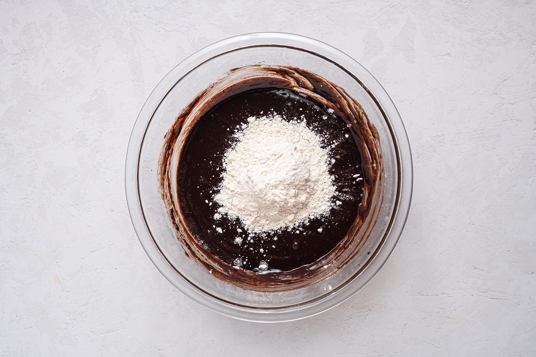 All-purpose flour sprinkled over the brownie batter, ready to be folded in gently.