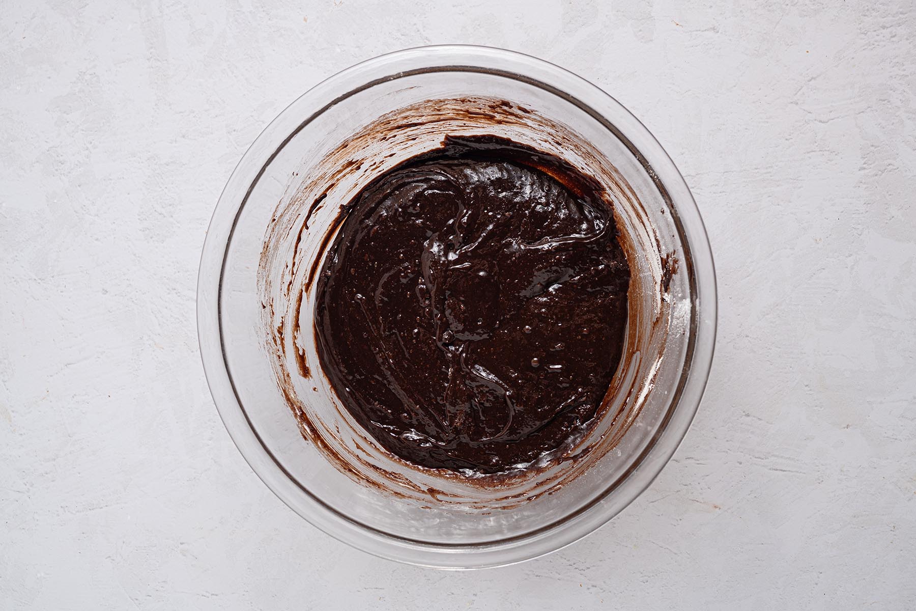 Thick, glossy brownie batter fully combined in a glass bowl, ready to spread into the pan.