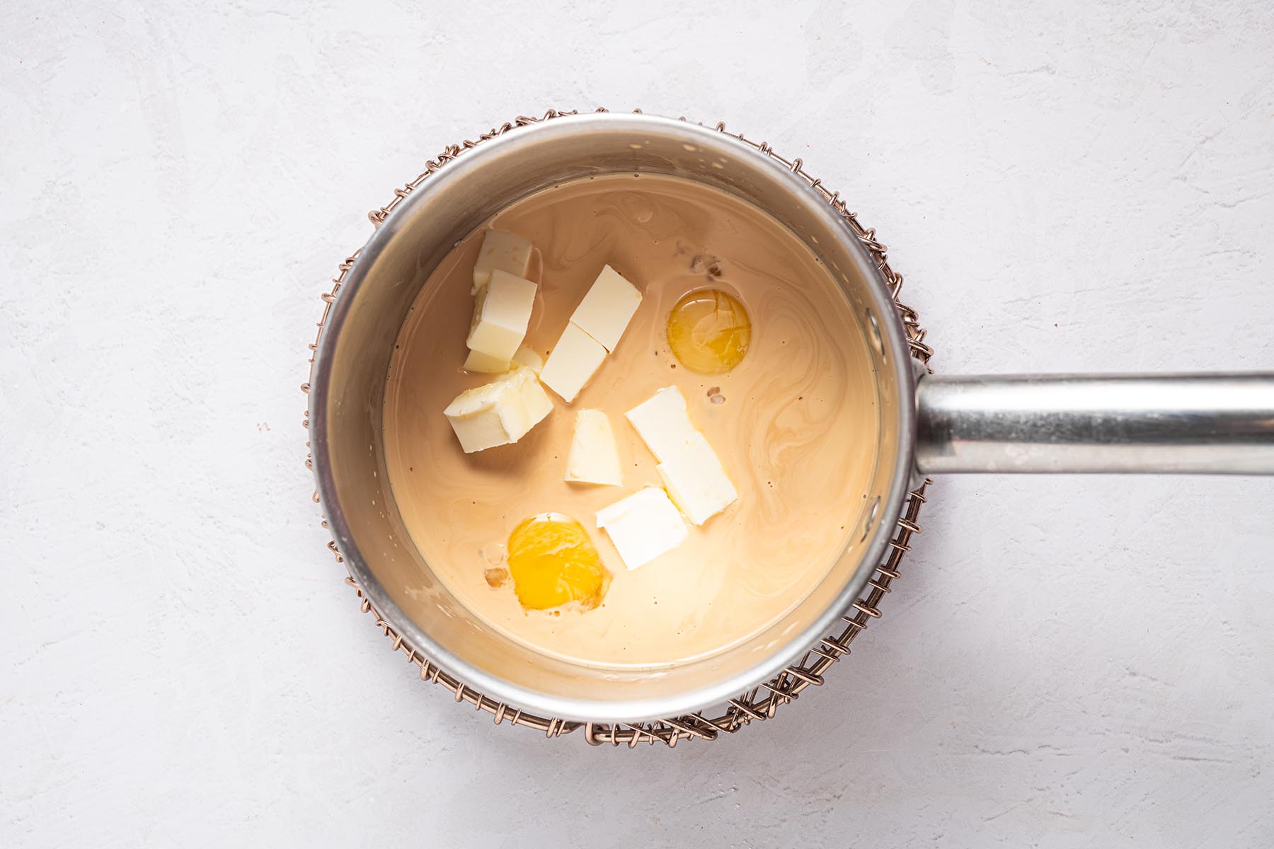 Evaporated milk, brown sugar, butter cubes, and two egg yolks in a saucepan before cooking the coconut-pecan frosting.