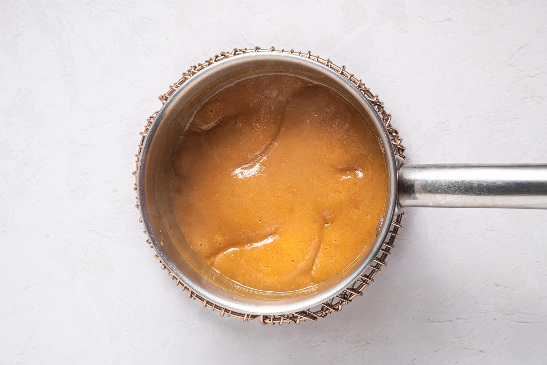 Caramel-colored frosting base bubbling and thickened in the saucepan, ready for mix-ins.