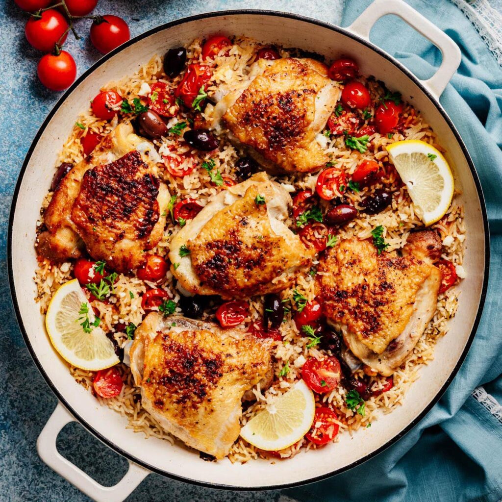Greek Chicken and Rice in a wide skillet&mdash;crispy thighs with tomatoes, Kalamata olives, parsley, and lemon.
