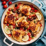 Greek Chicken and Rice in a wide skillet—crispy thighs with tomatoes, Kalamata olives, parsley, and lemon.
