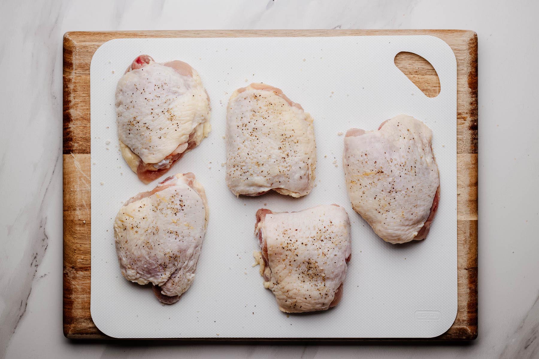 Seasoned bone-in chicken thighs on a cutting board, ready for searing for Greek Chicken and Rice.