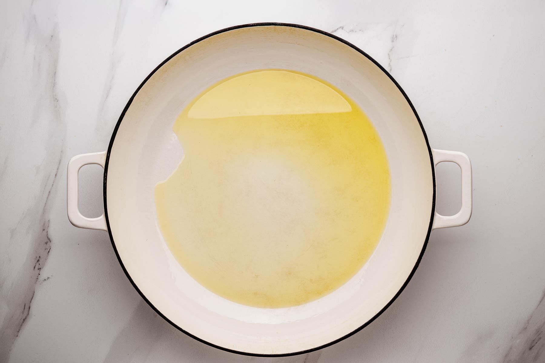 Olive oil heating in a wide enameled skillet to sear chicken for Greek Chicken and Rice.