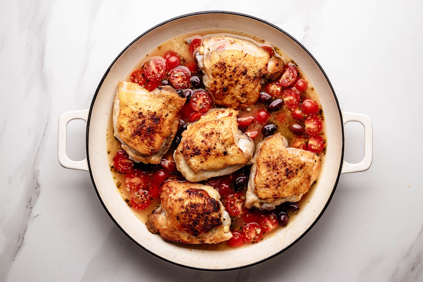 Seared chicken thighs nestled over tomato-olive rice, ready to simmer until tender.