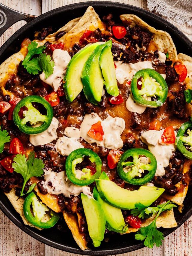 Loaded beef nachos topped with sliced avocado, jalape&ntilde;os, tomatoes, sour cream, and fresh cilantro served in a black skillet.