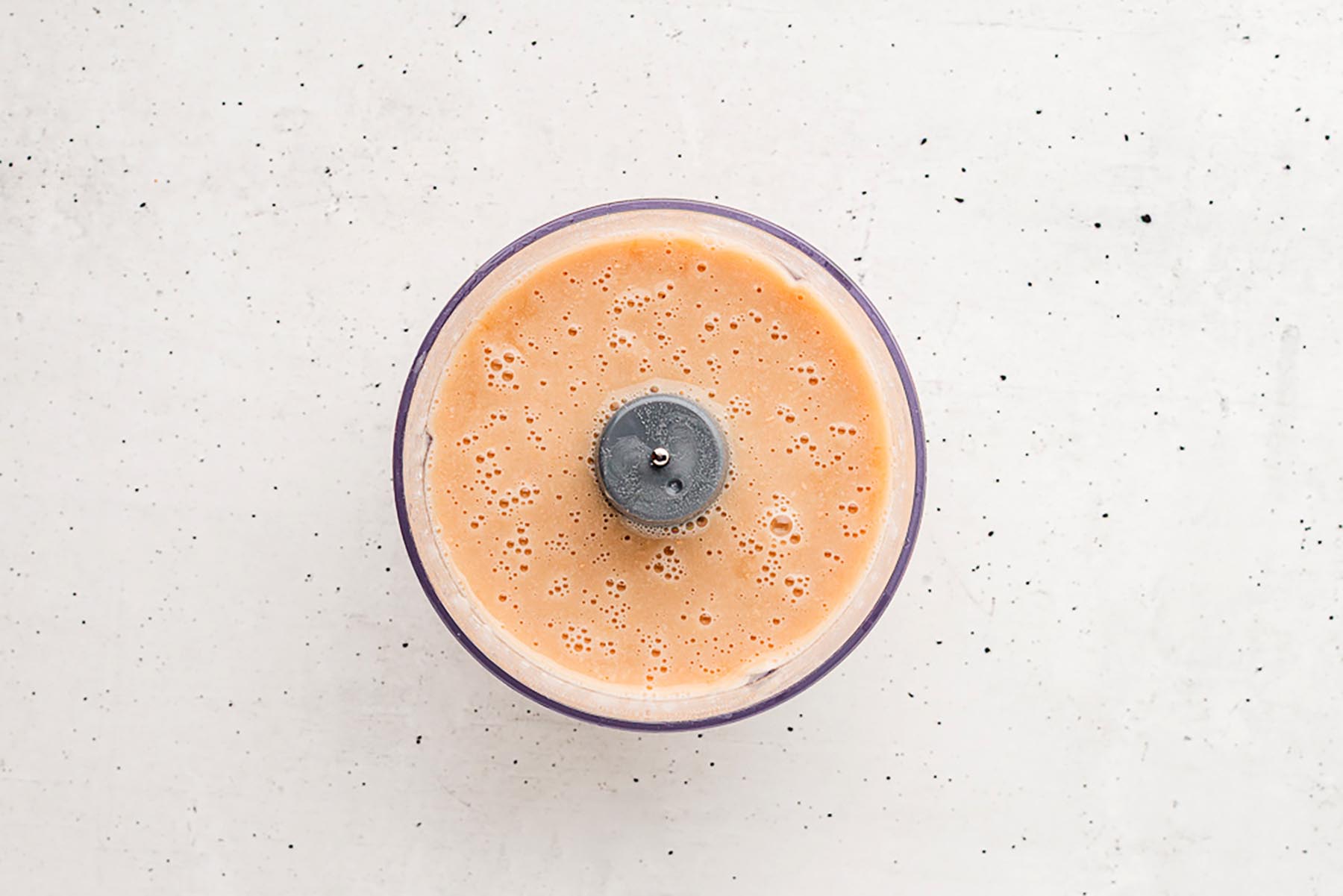 Overhead view of a food processor bowl filled with smooth blended white beans and broth, creating a creamy base for the soup.