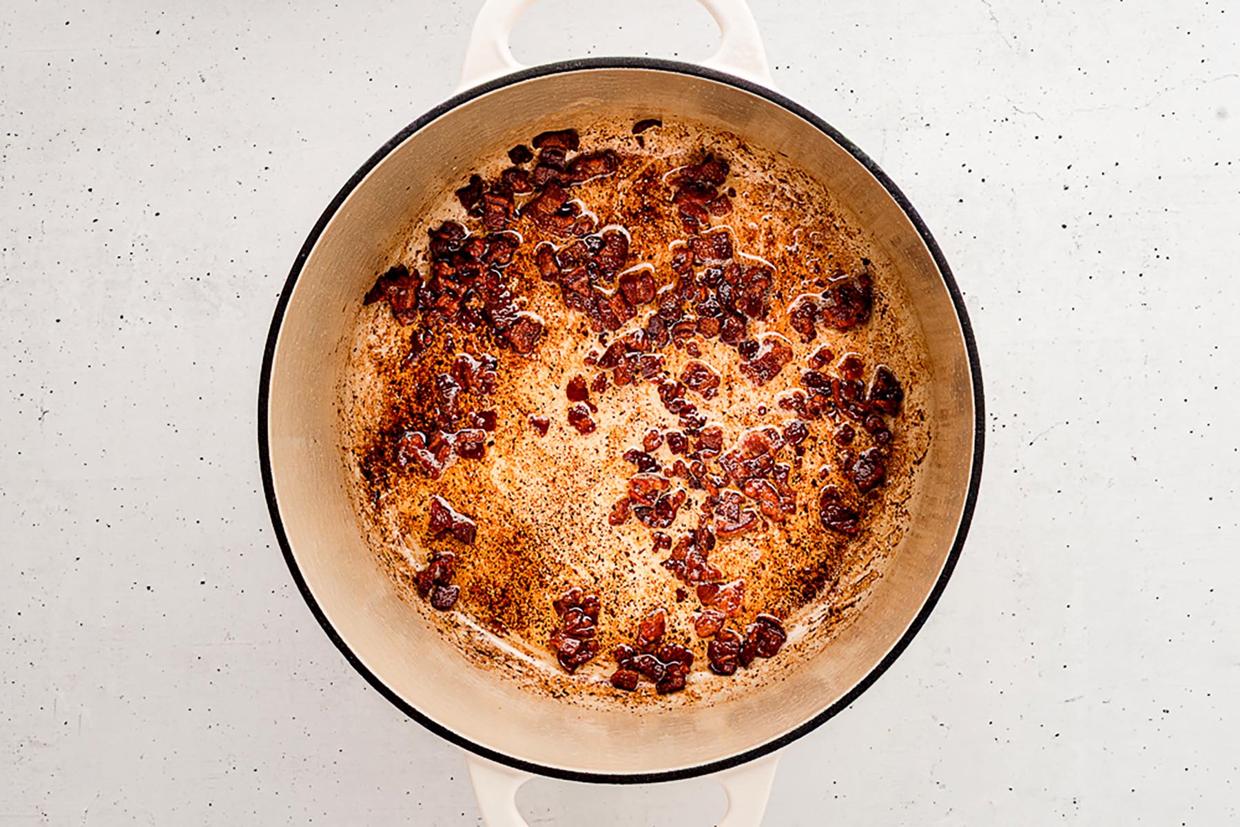 Overhead view of a Dutch oven with crisp browned bacon pieces and rendered fat on the bottom of the pot.